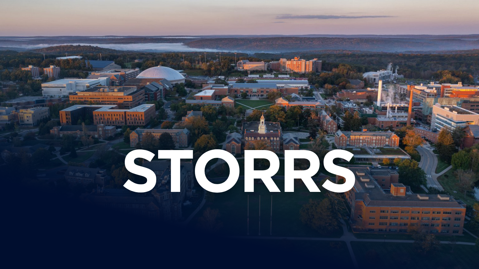 An aerial view of a sprawling university campus. The word "STORRS" is prominently displayed in large white letters across the bottom.