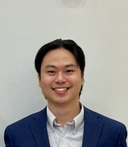 A headshot of a man wearing a suit in front of a white background.
